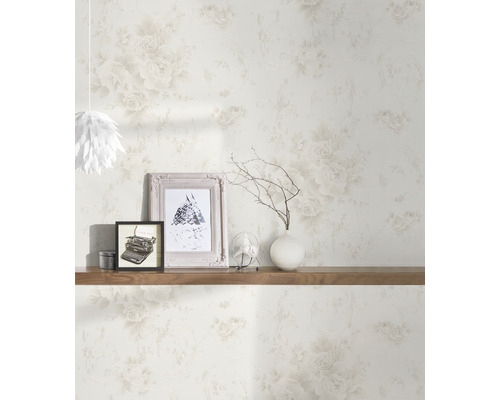 Vardagsrum med blommig tapet, dekorerad med bilder, en vas och en fläkt på en trähylla.