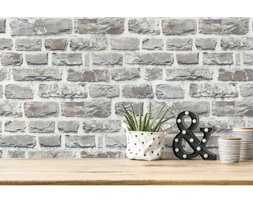 Dekorativ tapet i stenlook på en vägg med växt, dekorativt &-tecken och dekorativa burkar på ett bord