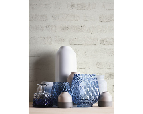 Dekorativa vaser av glas och keramik på ett bord framför en tegelvägg