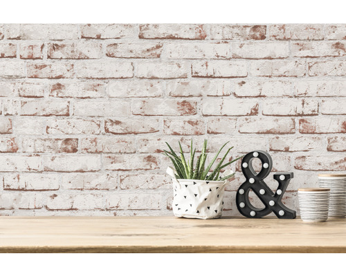 Dekorativ scen med växt, tecknet et och randig behållare framför en tegelvägg