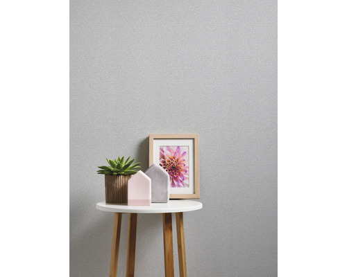 Närbild av en silverfärgad tapet med bord, växt, dekorativa hus och en fotoram