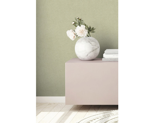 Närbild av en grön strukturtapet med en marmorvas och böcker på ett skåp