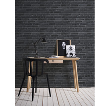 Skrivbord med stol, lampa och väggdekoration framför en tegelvägg