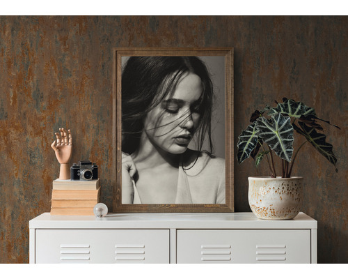 Dekorativ scen med inramat porträtt, växt i kruka, kameramodell och trähandske på ett vitt skåp.