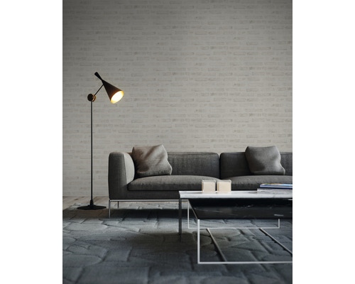 Vardagsrum med grå soffa, soffbord och golvlampa framför en tegelvägg