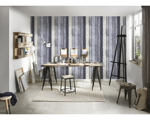 Ateljé med staffli, bord, pall och hylla framför en tapet med träutseende