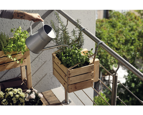 Vattenkanna som vattnar örter i en trälåda på en balkong.