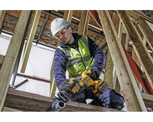 En byggnadsarbetare med skyddshjälm och skyddsglasögon sågar ett rör med en DeWalt tigersåg.