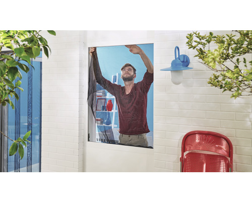 Man fäster ett insektsnät på ett fönster i ett ljust rum