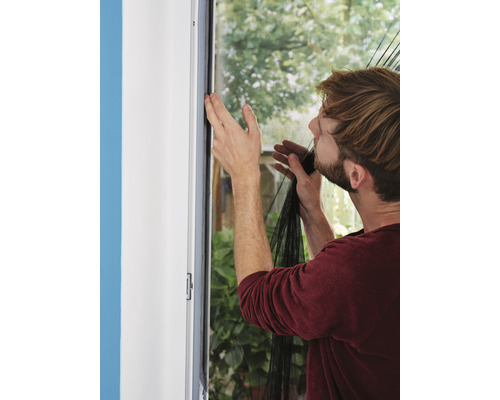 Man fäster ett insektsnät på en fönsterkarm.