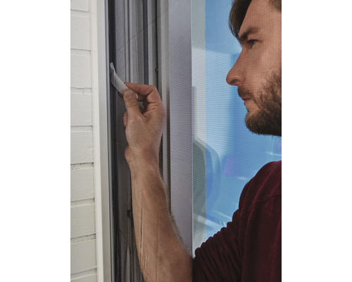 En man fäster ett myggnät på ett fönster.