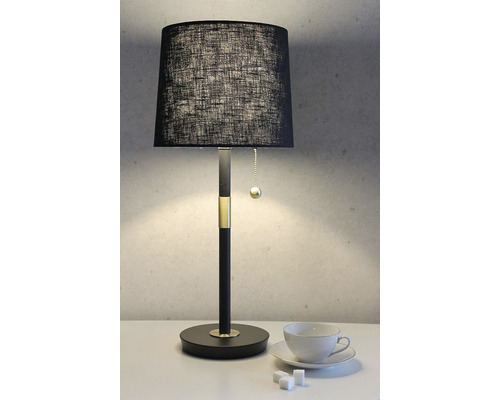 Bordslampa med svart lampskärm och en kopp på bordet