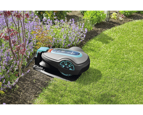 Gardena robotgräsklippare i trädgården på gräsmattan bredvid blomrabatter.