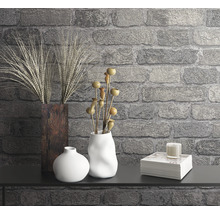 Dekorativ scen med vaser, växter, ljus och bokstapel mot en stenmur.