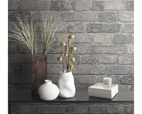 Dekorativ scen med vaser, växter, ljus och bokstapel mot en stenmur.