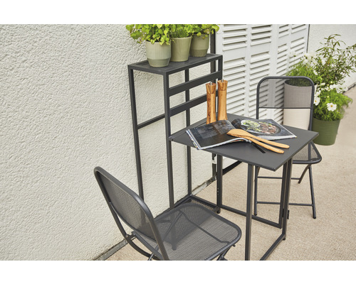 Trädgårdsscen med bord, två stolar och ett växtställ på en terrass.