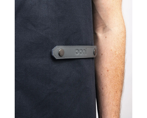 Detalj av ett grillförkläde med grå läderdetalj och Ooni logotyp.