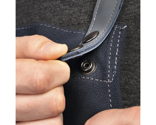 Närbild av en person som fäster en tryckknapp på ett blått arbetsförkläde.