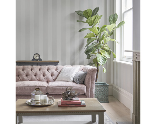 Vardagsrum med randig tapet, soffa, bord och krukväxt.