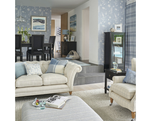 Ljust vardagsrum med blommig tapet, soffa, fåtölj, matbord och dekorationer