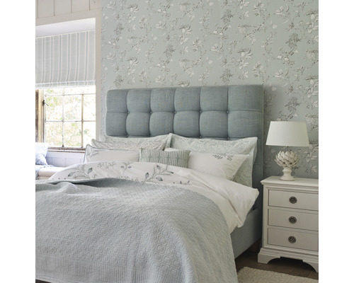 Sovrum med säng, sängbord och blommig tapet för en ljus och vänlig atmosfär