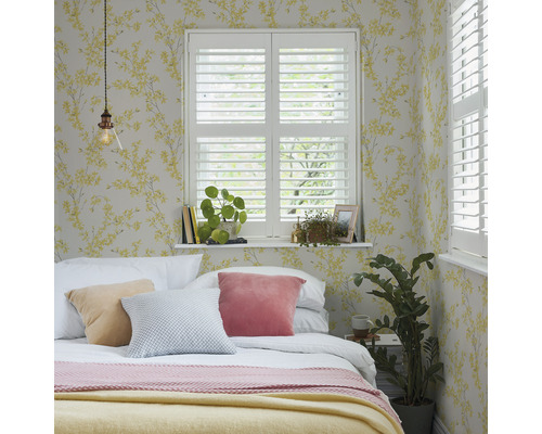 Sovrum med säng, kuddar, fönsterluckor och blommig tapet