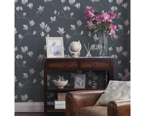 Vardagsrum med tapet med magnoliamönster, träkonsol, dekoration och läderfåtölj