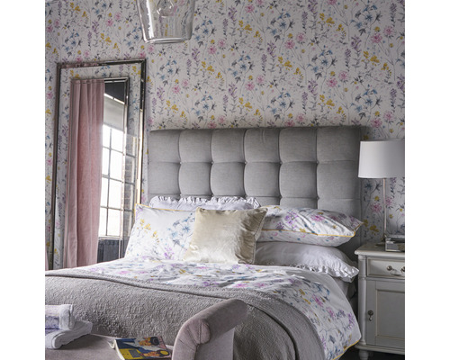Ljust sovrum med blommönstrad tapet, vadderad sänggavel och spegel