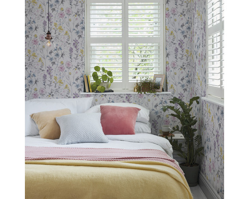 Sovrum med blommig tapet, säng, kuddar och fönster med fönsterluckor