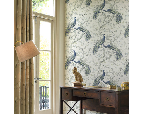 Ett arbetsrum med ett skrivbord i trä, en lampa och en tapet med ett påfågelmönster.