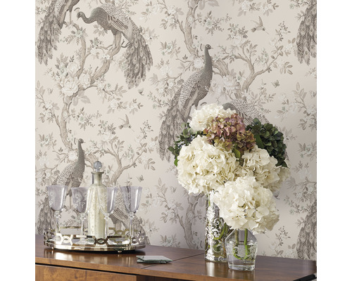 Interiör med mönstrad tapet med påfåglar, blommor, dryckesset på ett bord och blommor i vaser.