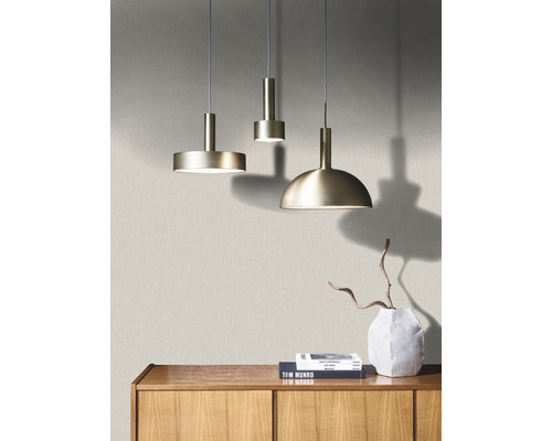 Tre metalliska hänglampor hänger ovanför ett träskåp med böcker och en vas.