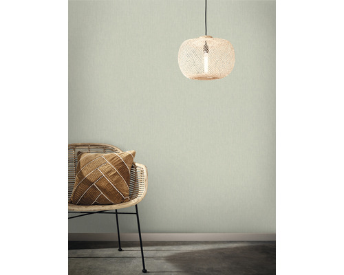 Rumsvy med rottingfåtölj, dekorativ kudde och rottinglampa framför en strukturerad väggtapet.