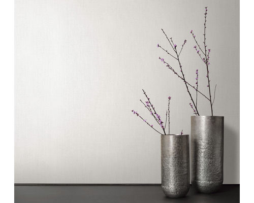 Två metallvaser med blommande grenar framför en vägg