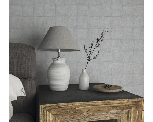 Dekorativt stilleben med lampa, vas och träskål på ett nattduksbord framför en strukturerad vägg