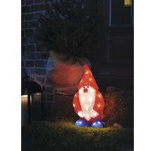 Dekorativ, upplyst tomte står framför en husentré bredvid en julgran.