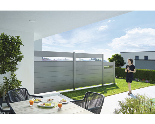 Terrass med insynsskydd, bord och stolar i trädgården.