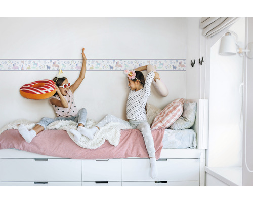 Barnrum med enhörningsbård och lekande barn på en säng med lådor