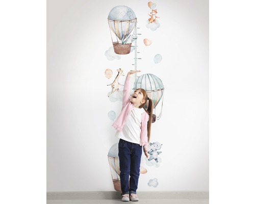 Flicka mäter sin längd med en väggdekal-mätsticka med luftballong- och djurmotiv