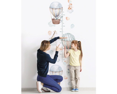 Mamma mäter ett barns längd med en väggdekal med luftballonger och djur.