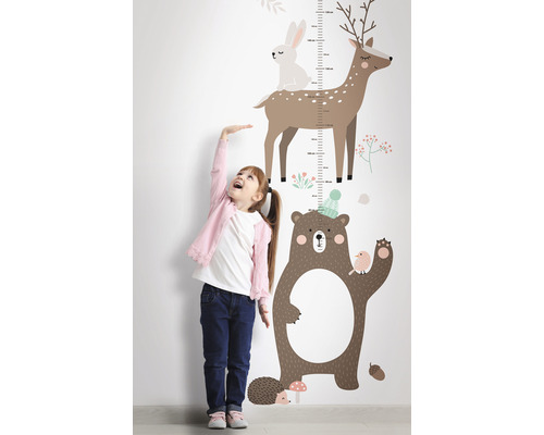 Flicka mäter sin längd bredvid en väggdekal med skogsdjursmotiv.
