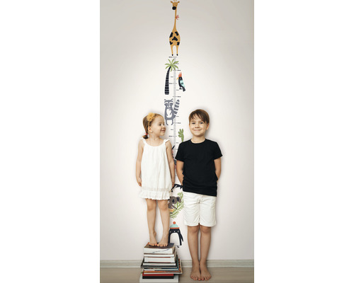 Två barn står framför en väggdekal med en tillväxtskala och djurmotiv.