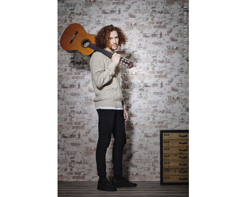 Man med gitarr framför en tegelvägg