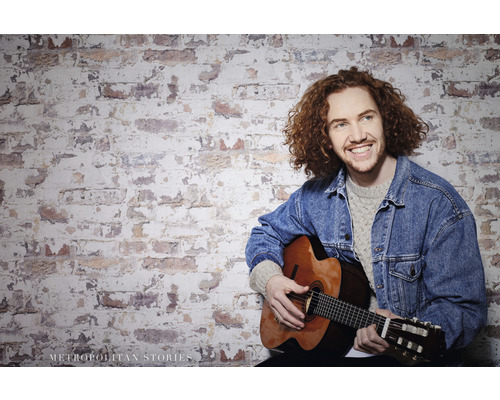 Man med gitarr framför en tegelvägg