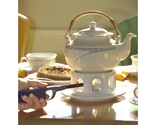 Tekanna på ett bord med kaka och en person som tänder ett värmeljus