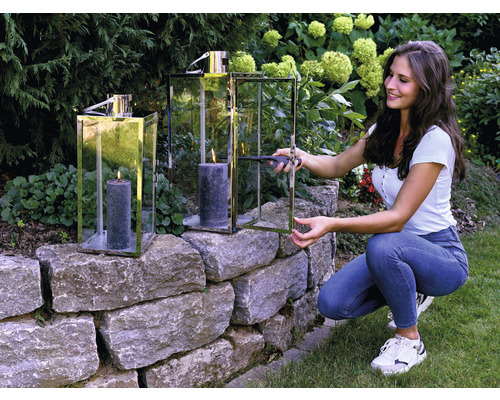 Kvinna tänder ljus i lykta på stenmur i trädgården