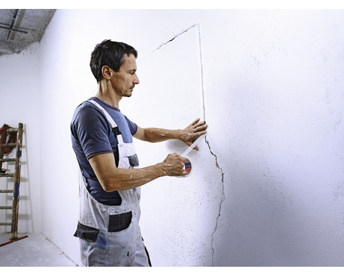 En man tejpar en vägg med maskeringstejp.