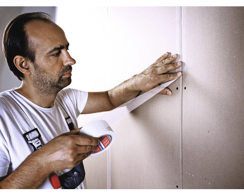 Man använder förstärkningsband på en gipsskiva.