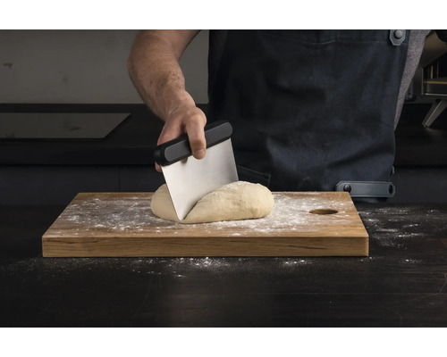 En person delar deg med en degskrapa på en träbräda.