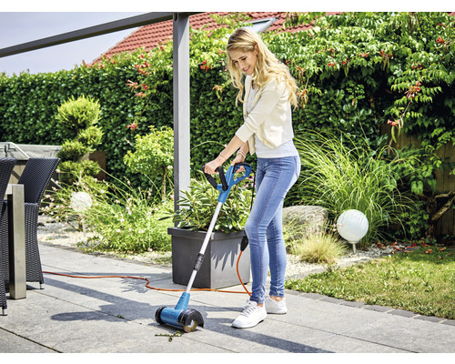 Kvinna använder en fogborste på en terrass för att ta bort ogräs.